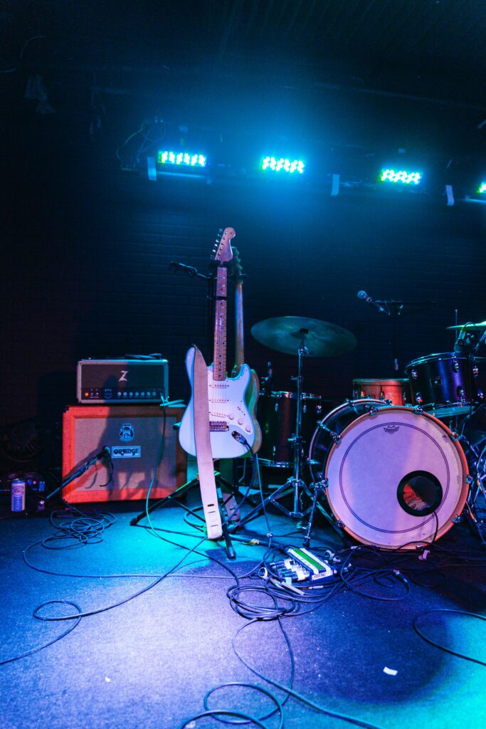 Electric guitar and drum set on an illuminated live music stage, ready for performance.